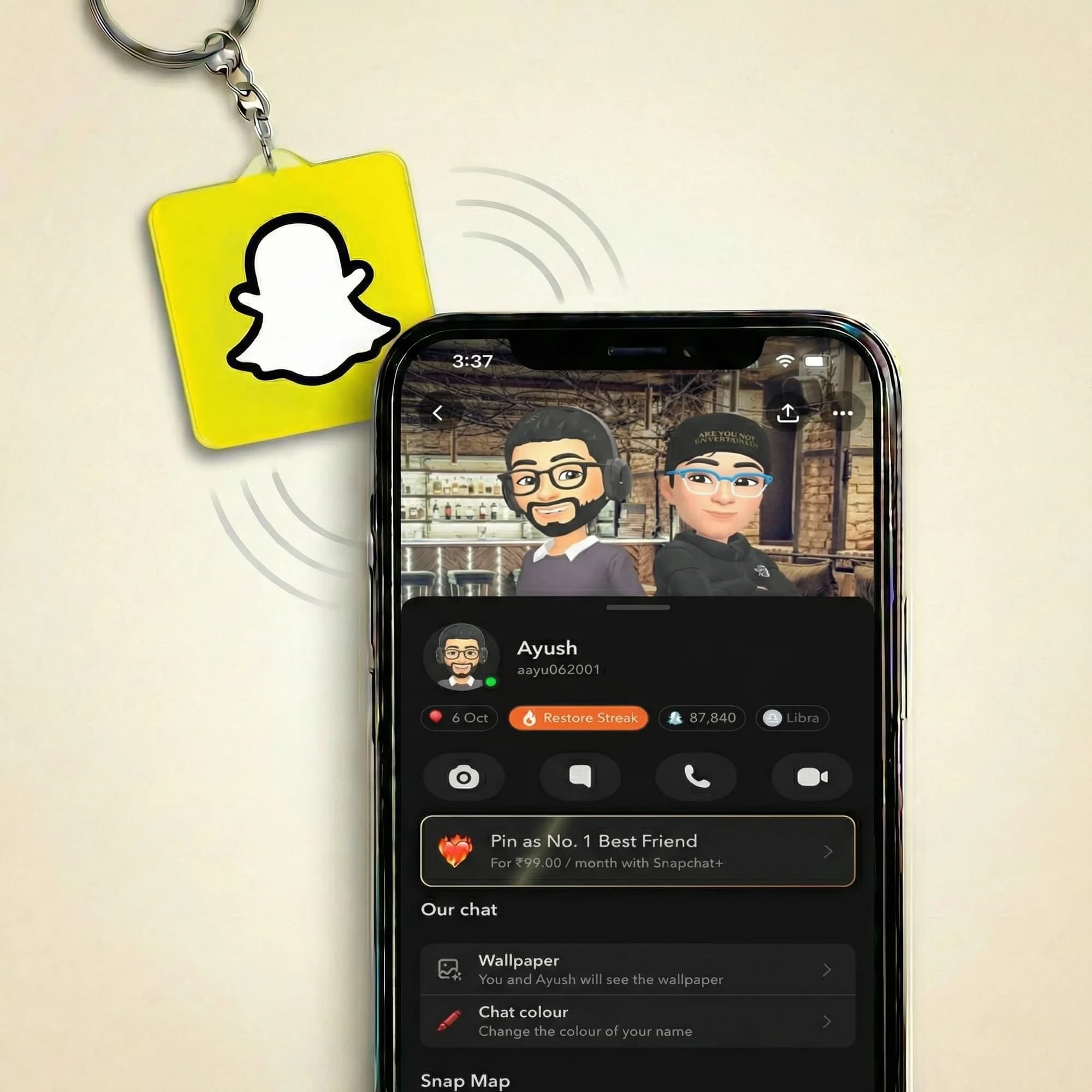 A yellow keychain with the Snapchat logo hangs next to a smartphone displaying a Snapchat profile.