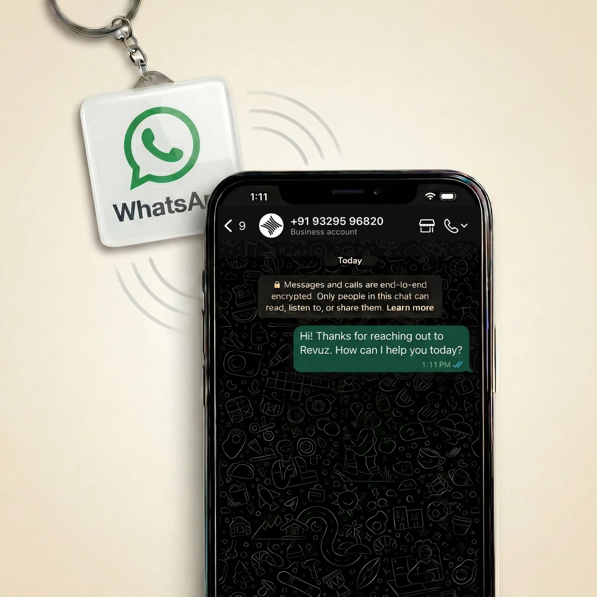 A square keychain with a WhatsApp logo hangs next to a smartphone displaying a WhatsApp chat.