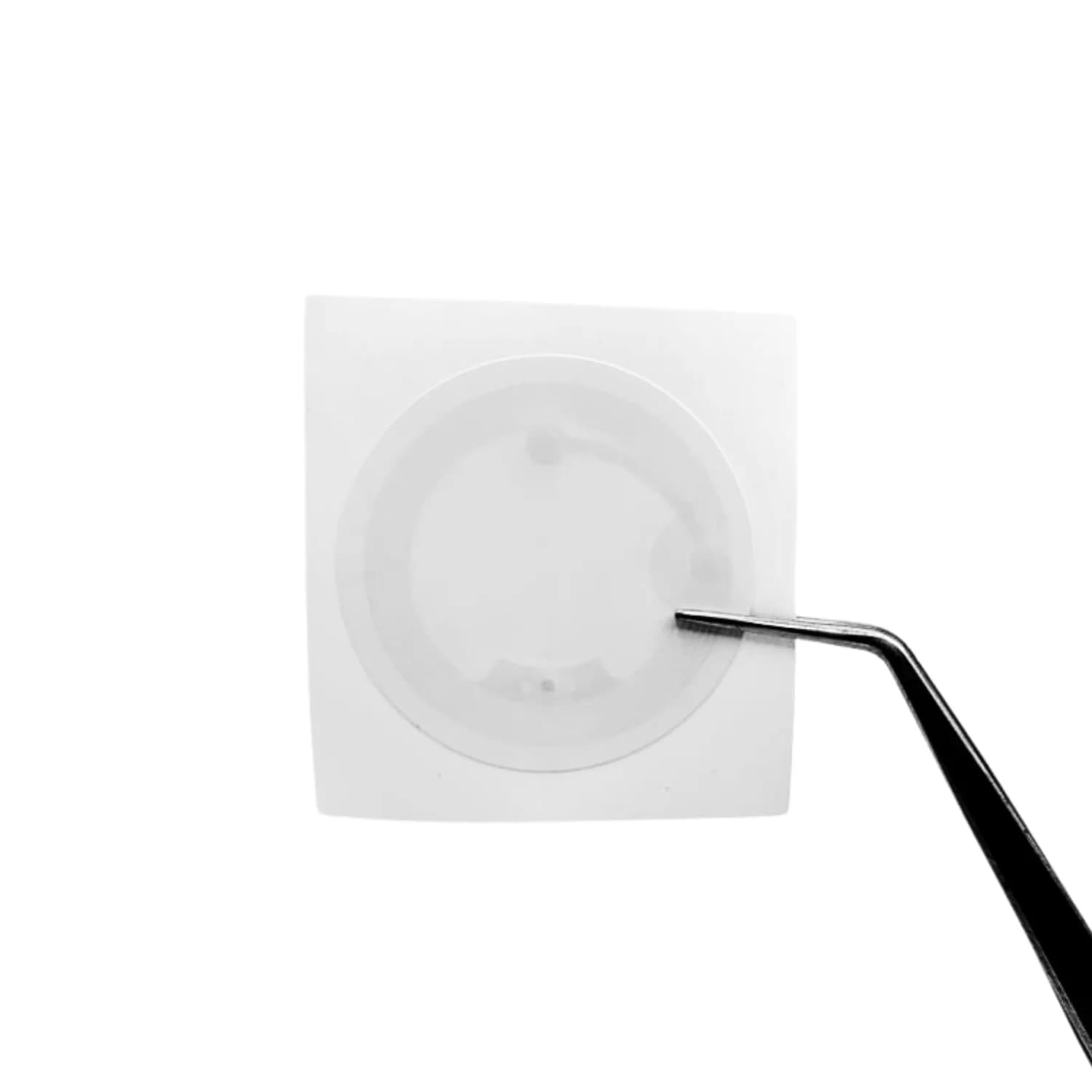 A white circular NFC sticker held by tweezers against a plain background.
