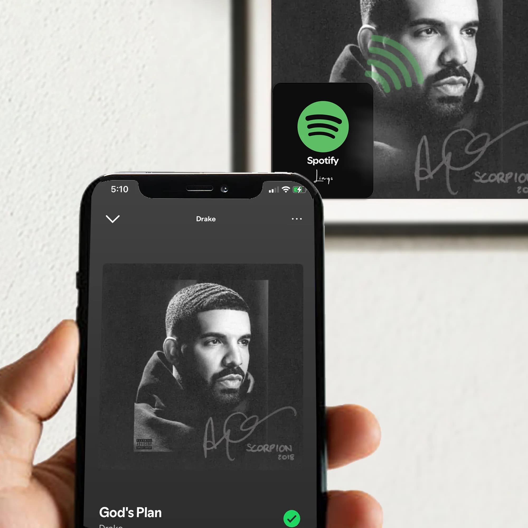 A hand holds a phone displaying a music app near a framed photo with a Spotify sticker.