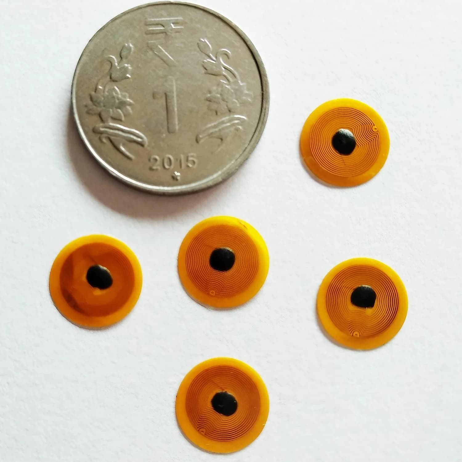 Five small, round yellow NFC stickers with a black center next to a coin on a white surface.