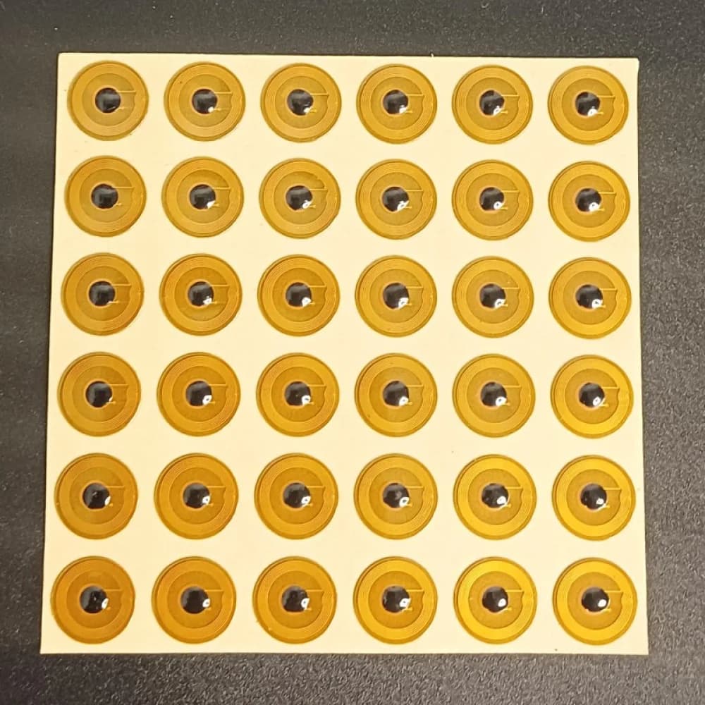 A grid of small, round, gold-colored NFC stickers on a dark surface.