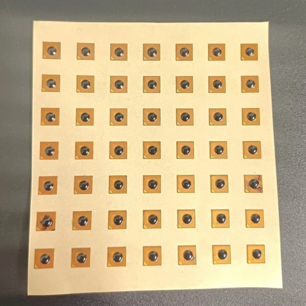 A grid of small, square, gold-colored NFC stickers with black centers on a beige sheet.