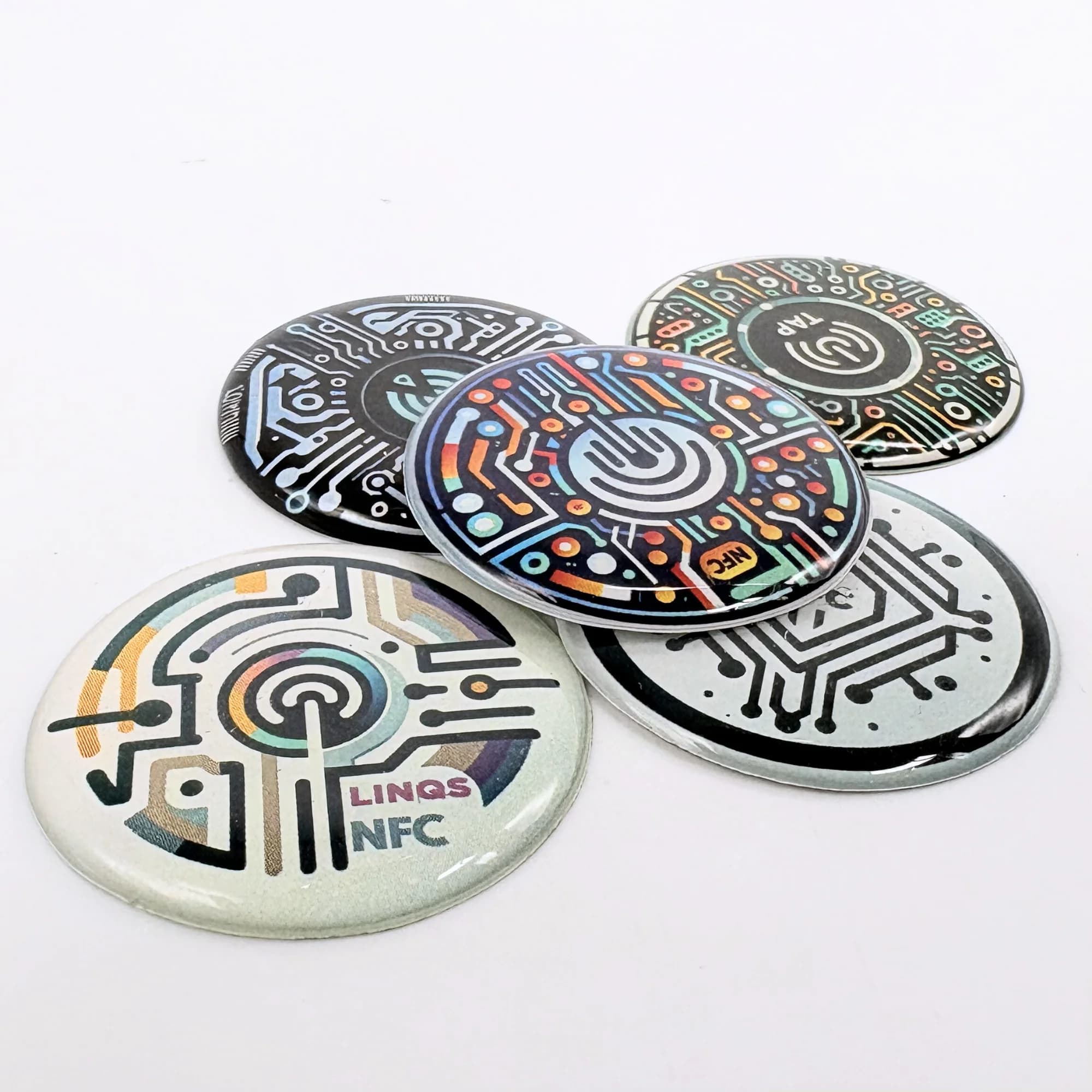 Five colorful LINQS NerdiTags NFC stickers with circuit designs are arranged on a white surface.