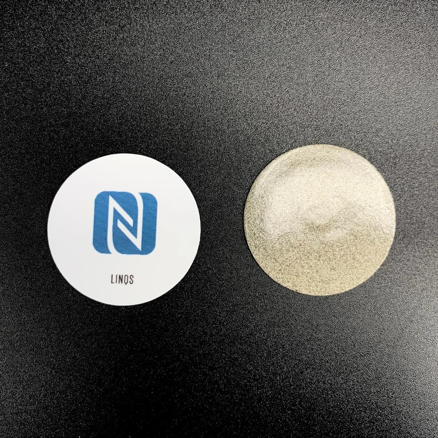 Two round stickers on a black surface: one white with a blue NFC logo and "LINQS" text, the other metallic.