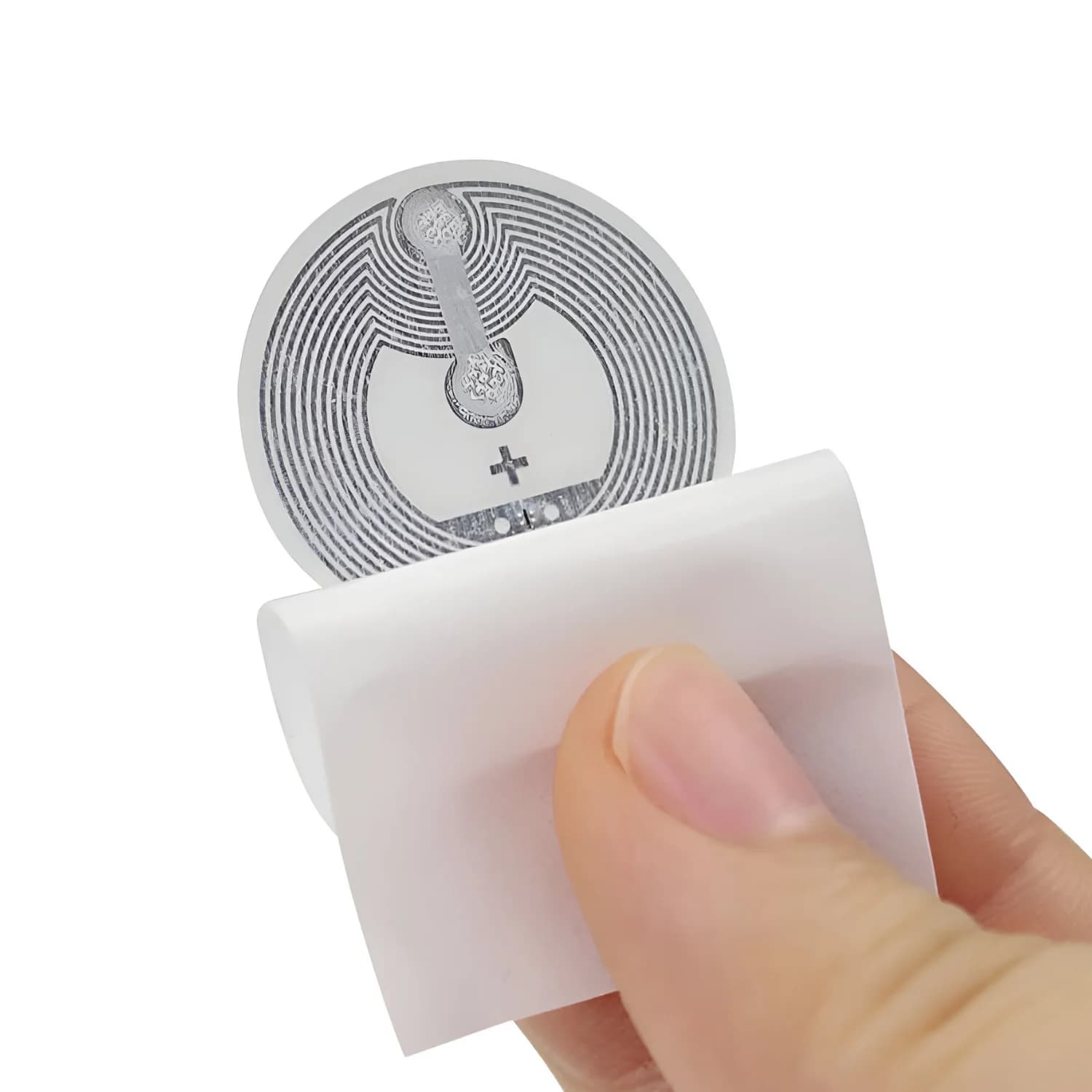 A hand holding a plain white circular NFC sticker with visible circuitry on the back.
