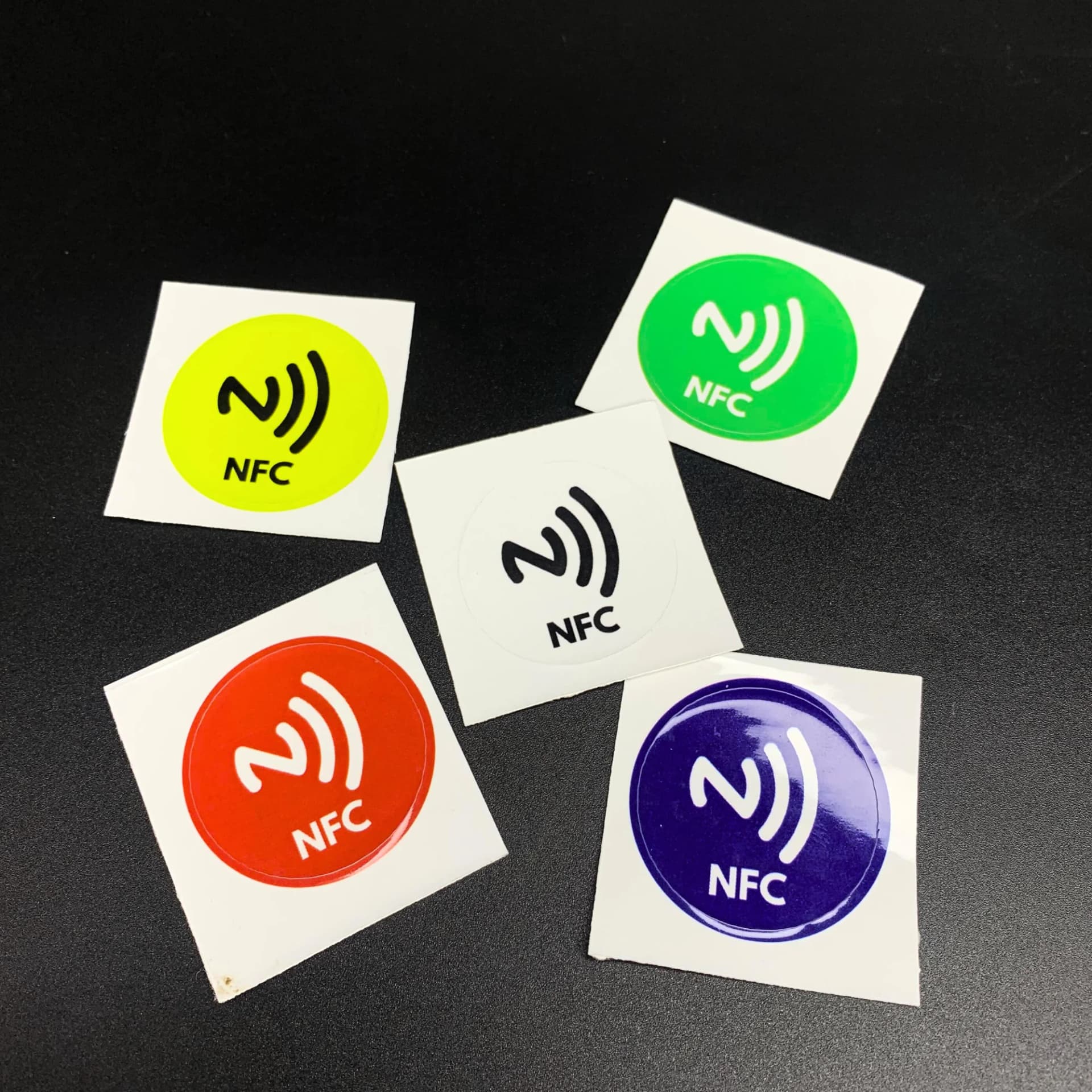 Colorful round NFC stickers with white NFC symbols and "NFC" text on a black background.
