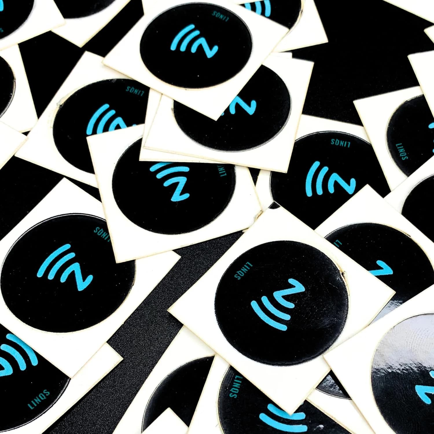 Multiple black and white circular NFC stickers with blue logo and text, scattered on a dark surface.