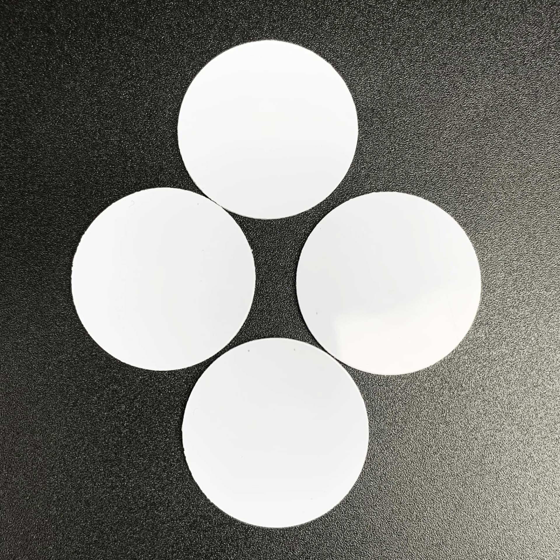 White circular NFC coin tags with a smooth surface, placed on a black textured background.