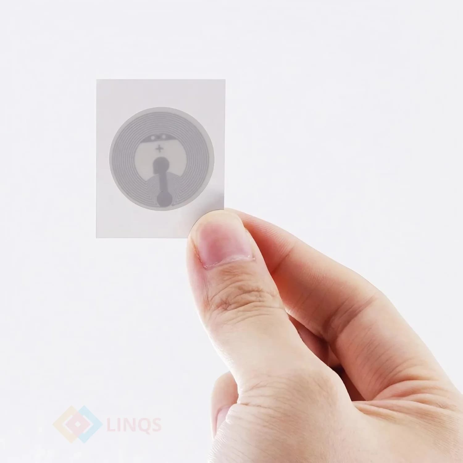 A hand holds a transparent square sticker with a visible circular NFC chip design.