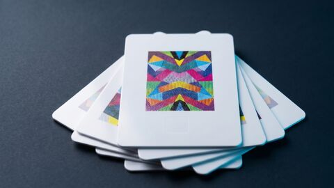 Fan of CR80 PVC NFC cards on dark slate, top card showing a full-colour CMYK printed pattern.